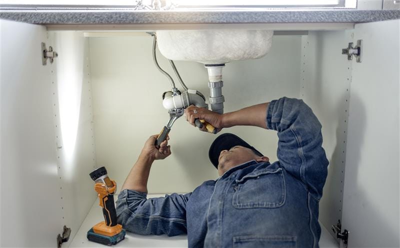 Plumber repairing pipes beneath a bathroom sink in Littleton