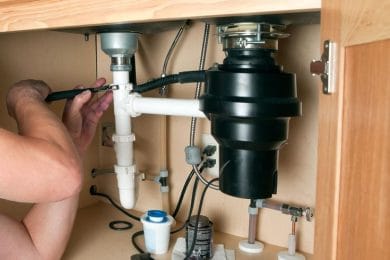 Plumber repairing a garbage disposal beneath a kitchen sink in Littleton
