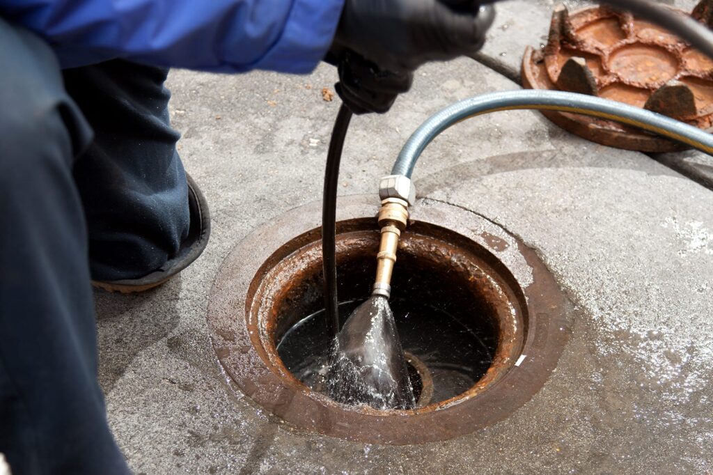 Plumber hydro jetting a sewer line through a manhole in Littleton