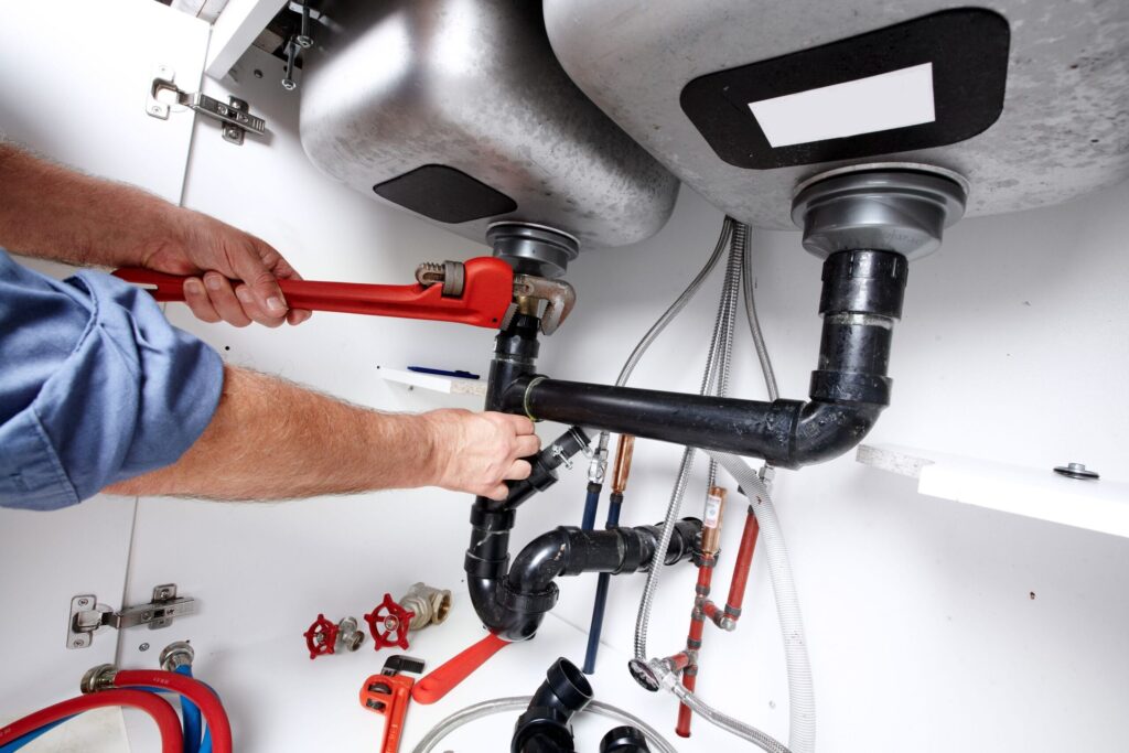 Plumber repairing drain pipes beneath a kitchen sink in Littleton